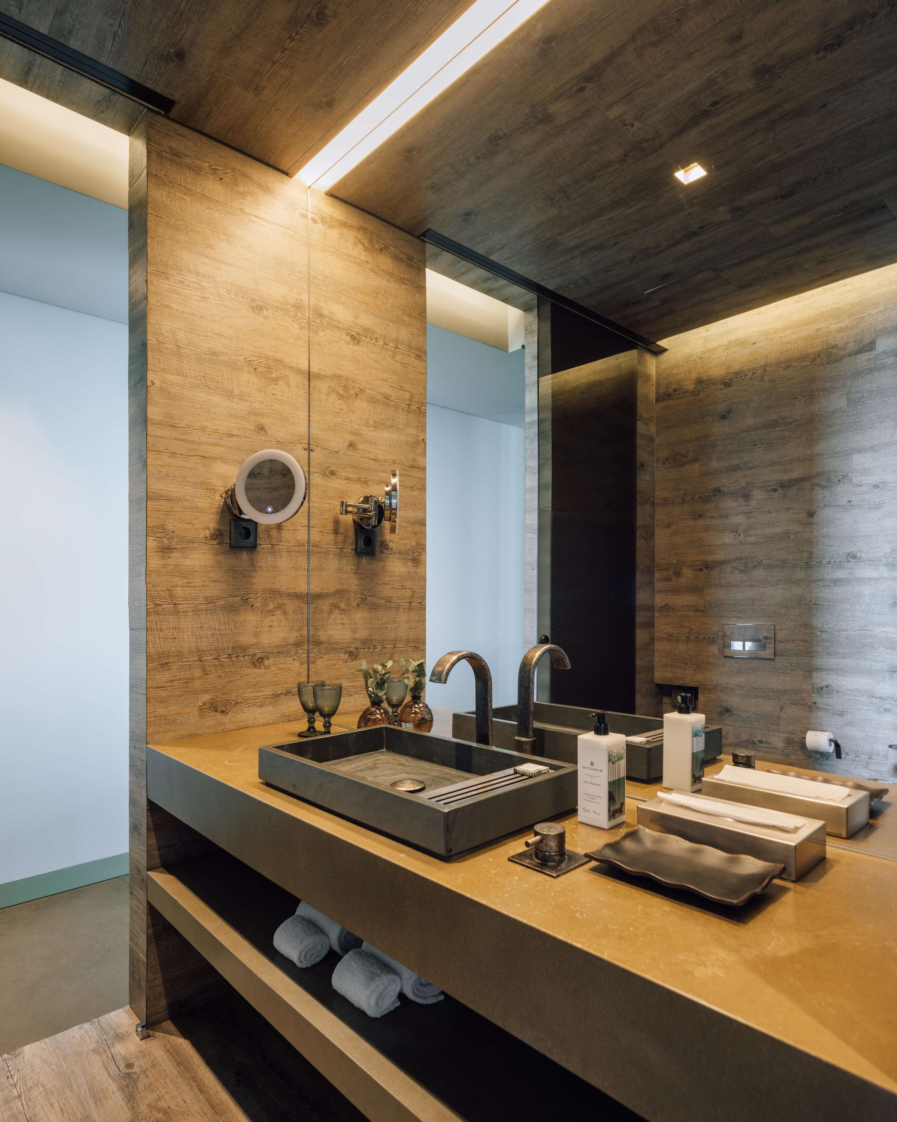 A modern bathroom with a wooden vanity, two sinks, a large mirror, and built-in shelves.