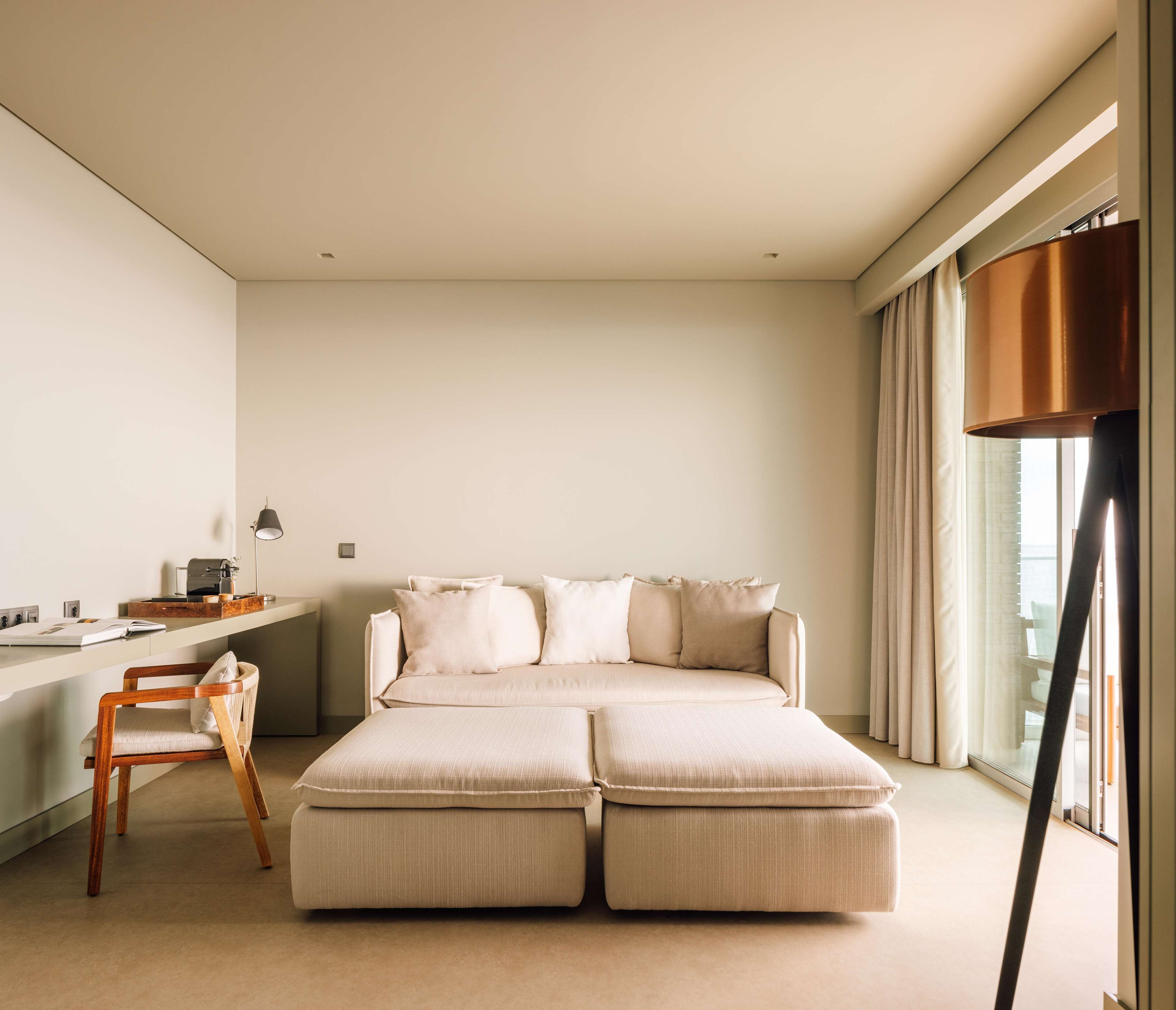 A modern bedroom with a large sofa bed, a desk with a lamp, and a chair.