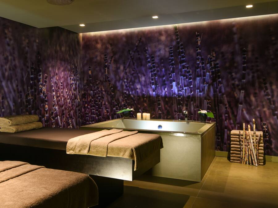Une salle de spa moderne dotée d’une grande baignoire, d’une table de massage et d’un mur orné de décorations verticales évoquant le bambou.