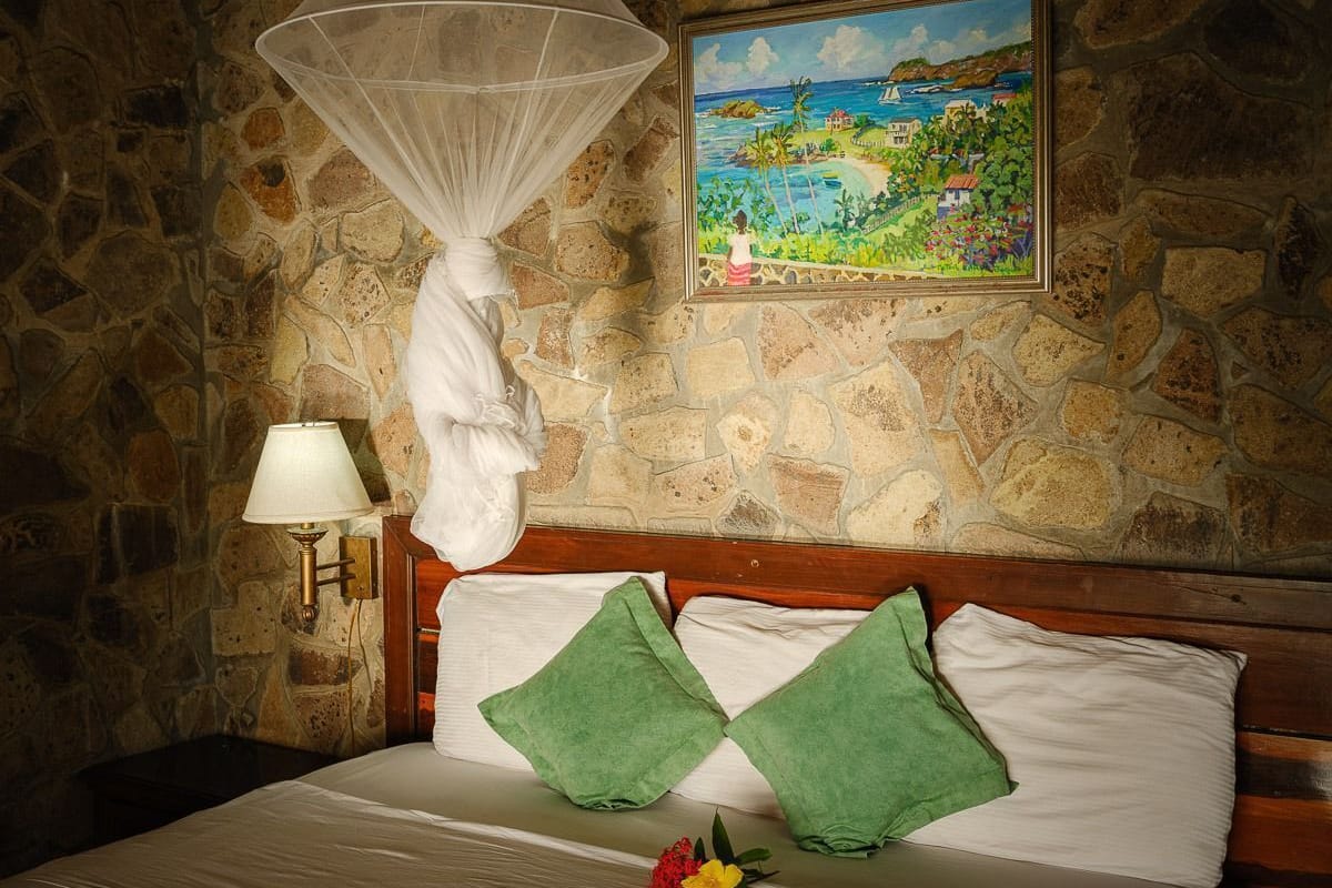 A bed with a stone wall backdrop, a painting of a coastal scene, and a bedside lamp.