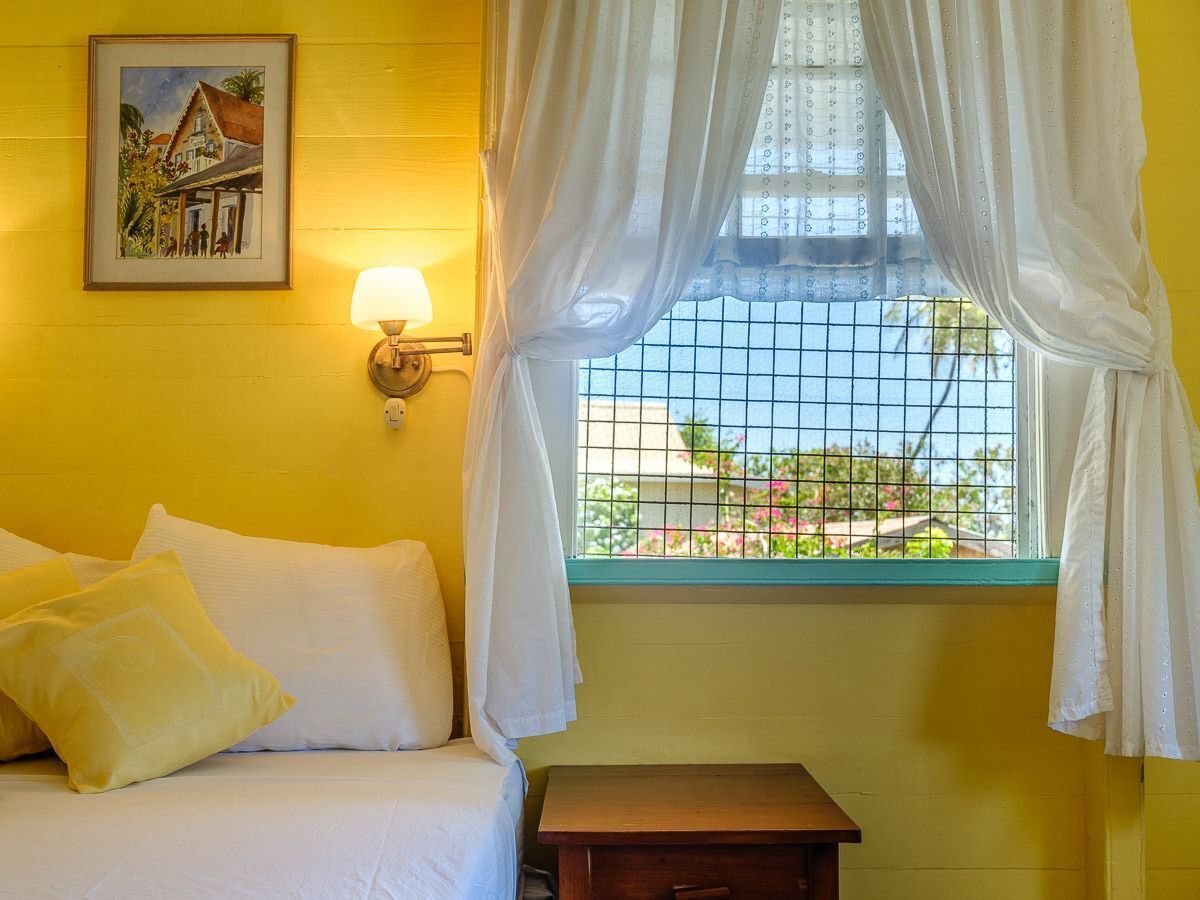 Une chambre avec un lit, une table de chevet, une lampe fixée au mur et une fenêtre avec des rideaux.