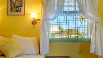 A room with a bed, a nightstand, a wall-mounted lamp, and a window with curtains.