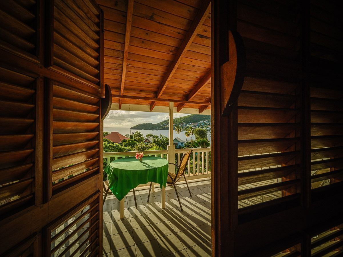 Un balcon en bois, agrémenté d’une table et de chaises, qui offre une vue panoramique sur un plan d’eau et des collines.