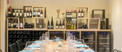 A dining area with a long table set for a meal, surrounded by wine racks and shelves with bottles.
