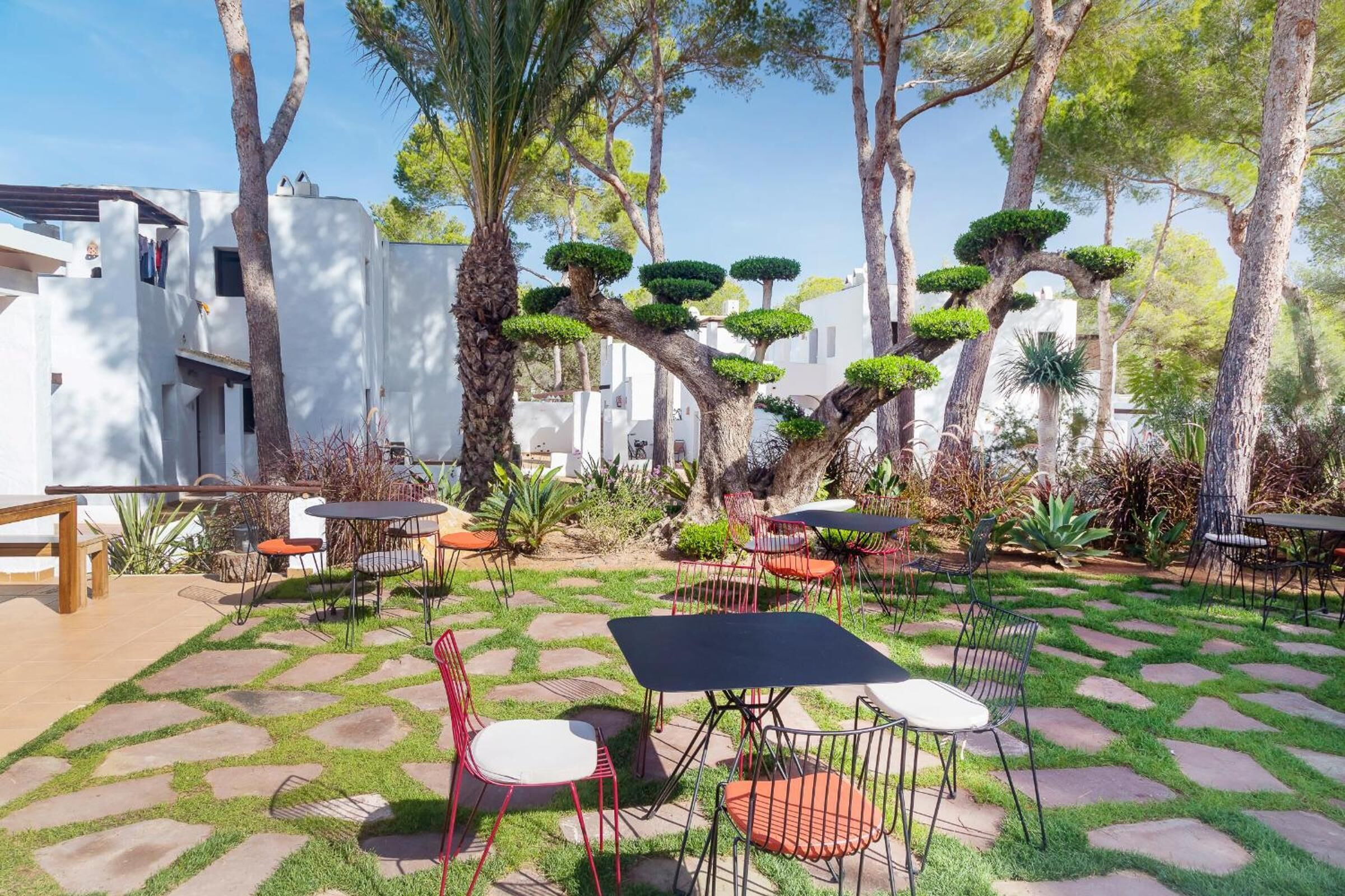 Eine Terrasse im Freien mit Steinboden, roten und weißen Stühlen und Tischen.
