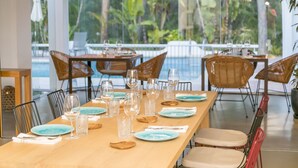 A dining area with a long table set for multiple guests, surrounded by chairs, and overlooking a pool with lush greenery. - Casbah Formentera Hotel & Restaurant (Formentera)