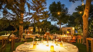An outdoor dining area with round tables set for a meal, surrounded by trees and a building in the background. - Casbah Formentera Hotel & Restaurant (Formentera)