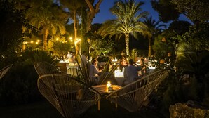An outdoor dining area with wicker chairs and tables, surrounded by palm trees and illuminated by string lights. - Casbah Formentera Hotel & Restaurant (Formentera)
