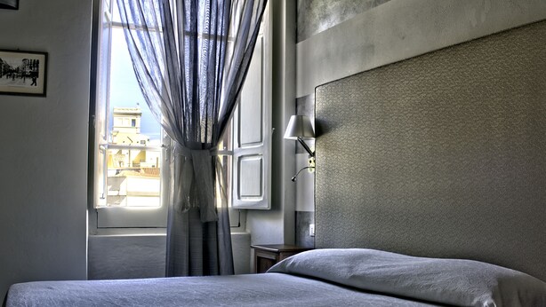 Een hotelkamer met een bed, een raam met gordijnen, een lamp en een wandlamp.