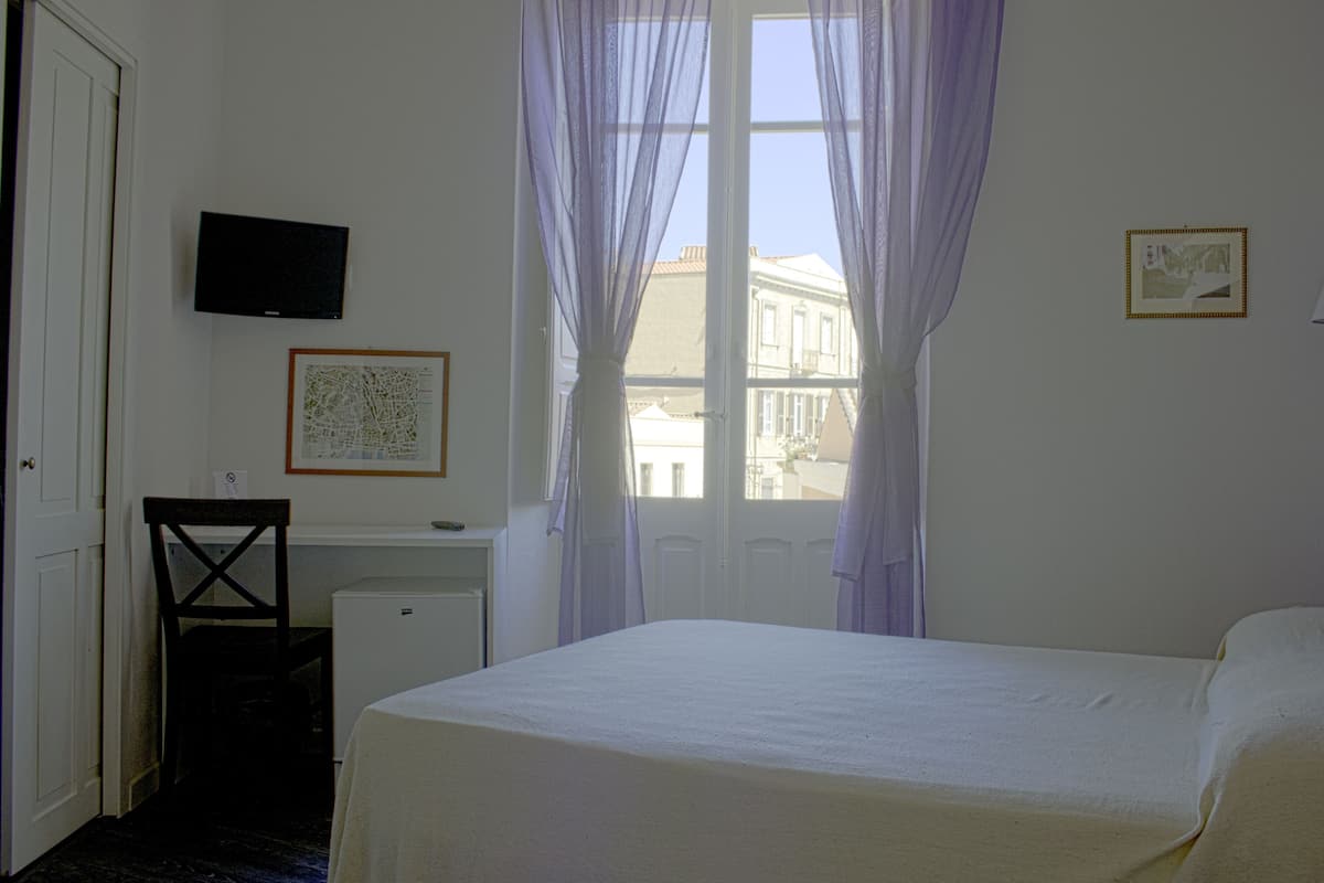 Une chambre d’hôtel comprenant un lit, un bureau avec une chaise, une télévision et une fenêtre avec des rideaux.