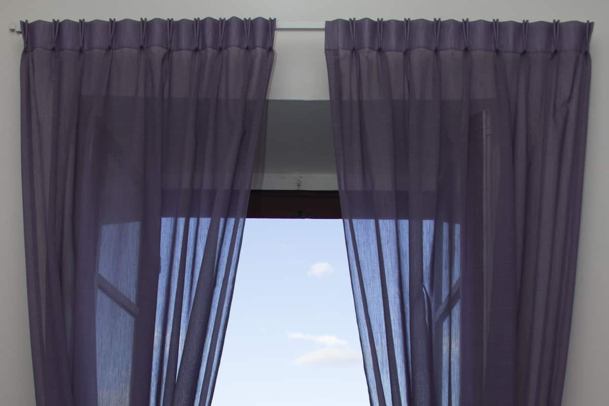 Une fenêtre avec des rideaux violets, un balcon avec une table, et des bâtiments en arrière-plan.