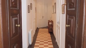 Een hal met geruit vloerkleed, houten deuren en wanden met ingelijste foto’s.