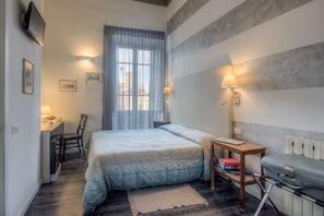A bedroom with a bed, a desk with a chair, a lamp, and a suitcase. - Al Bastione di Cagliari (Cagliari)