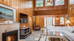 A cozy cabin interior with a fireplace, wooden walls, a sofa, and a dining area.