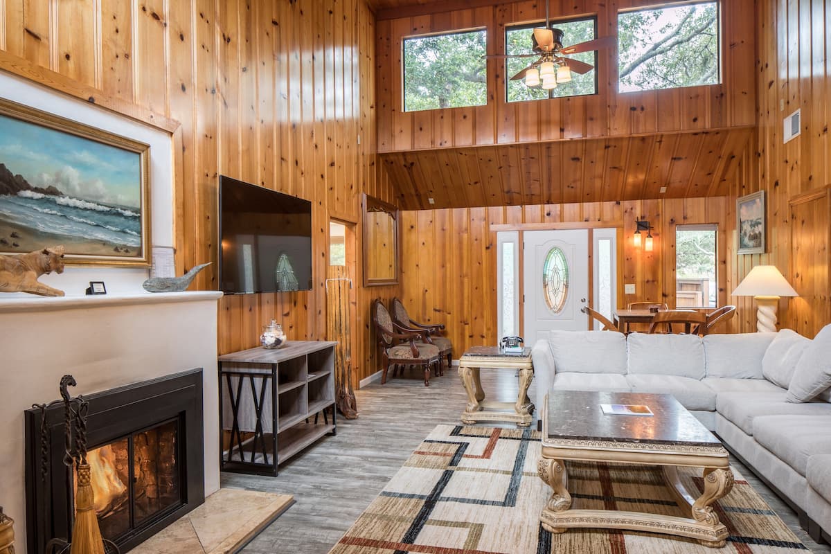 A cozy cabin interior with a fireplace, wooden walls, a sofa, and a dining area.