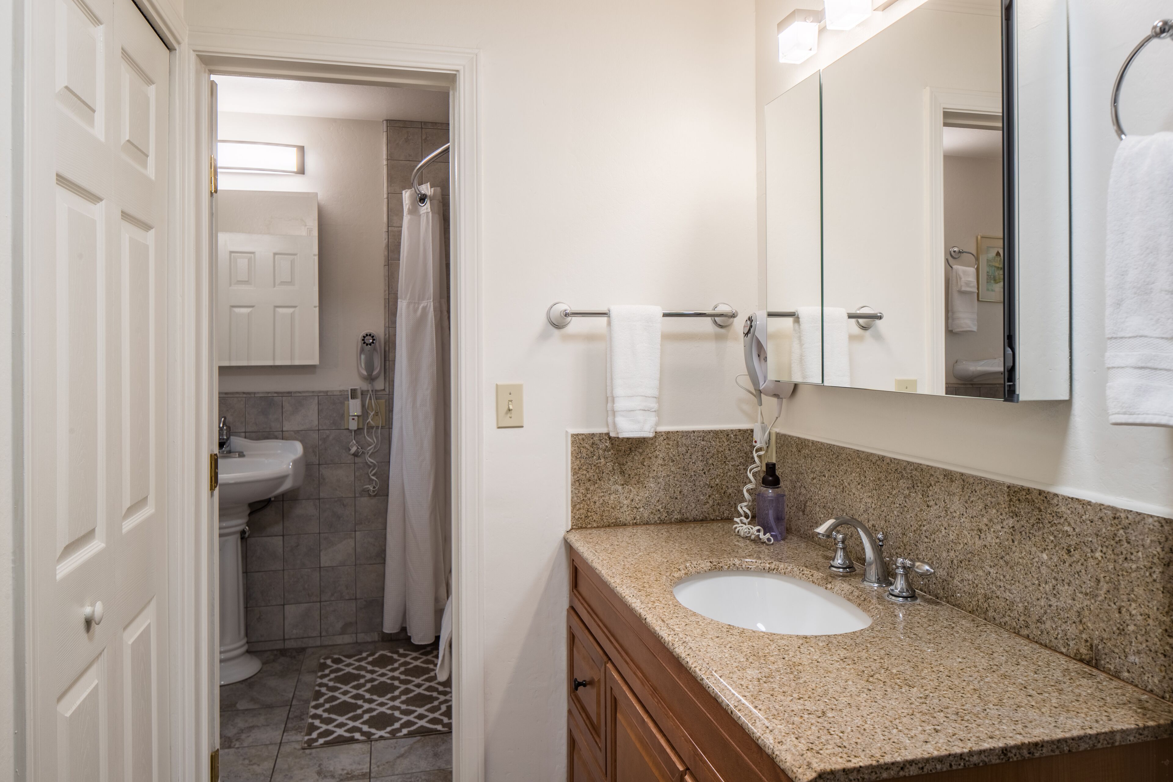 A bathroom with a sink, mirror, towel rack, and shower.