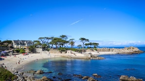 A coastal beach with clear blue waters, a sandy shore, and a stone wall.