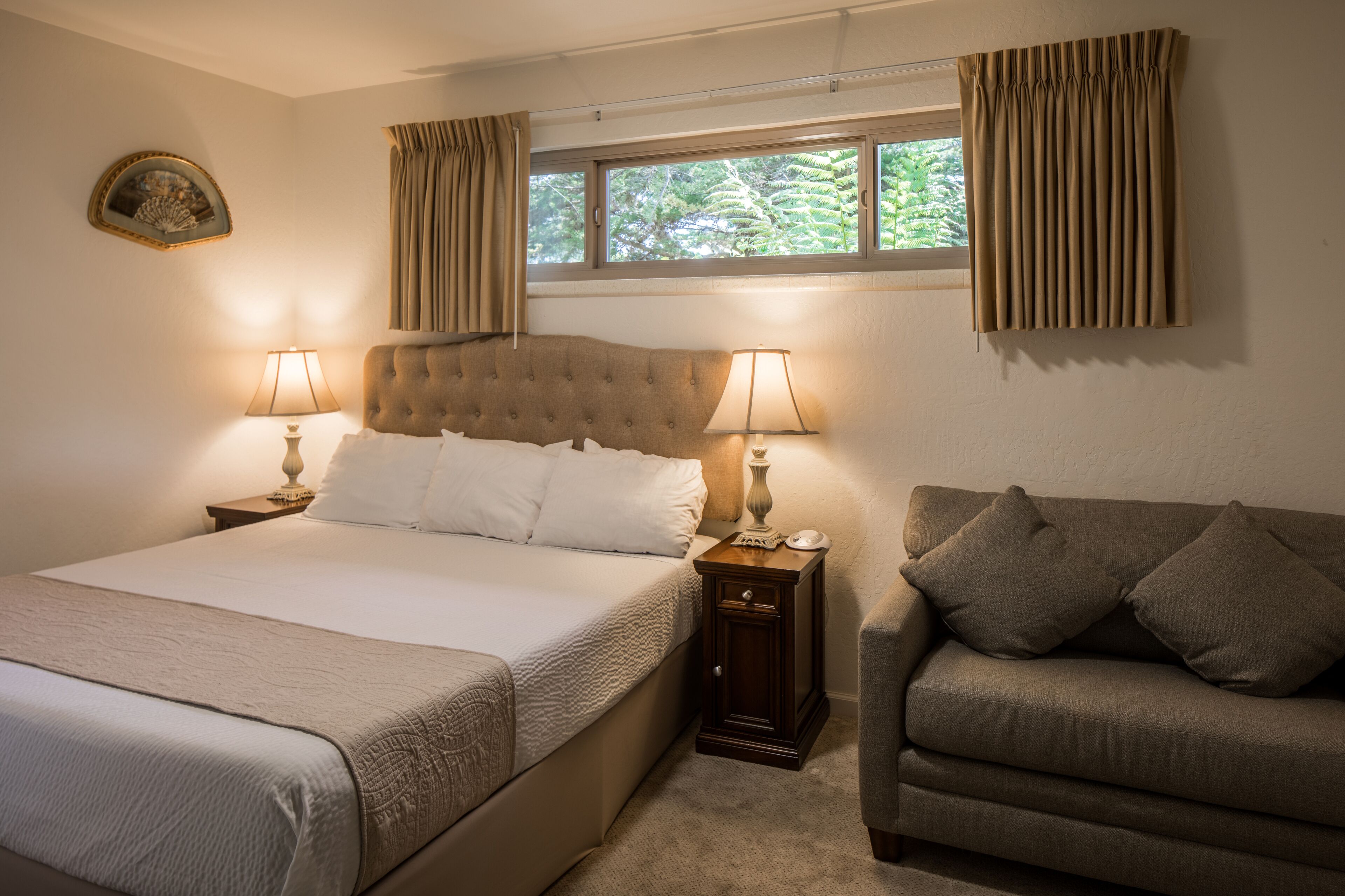 A bedroom with a large bed, two bedside tables with lamps, a sofa, and a window with curtains.