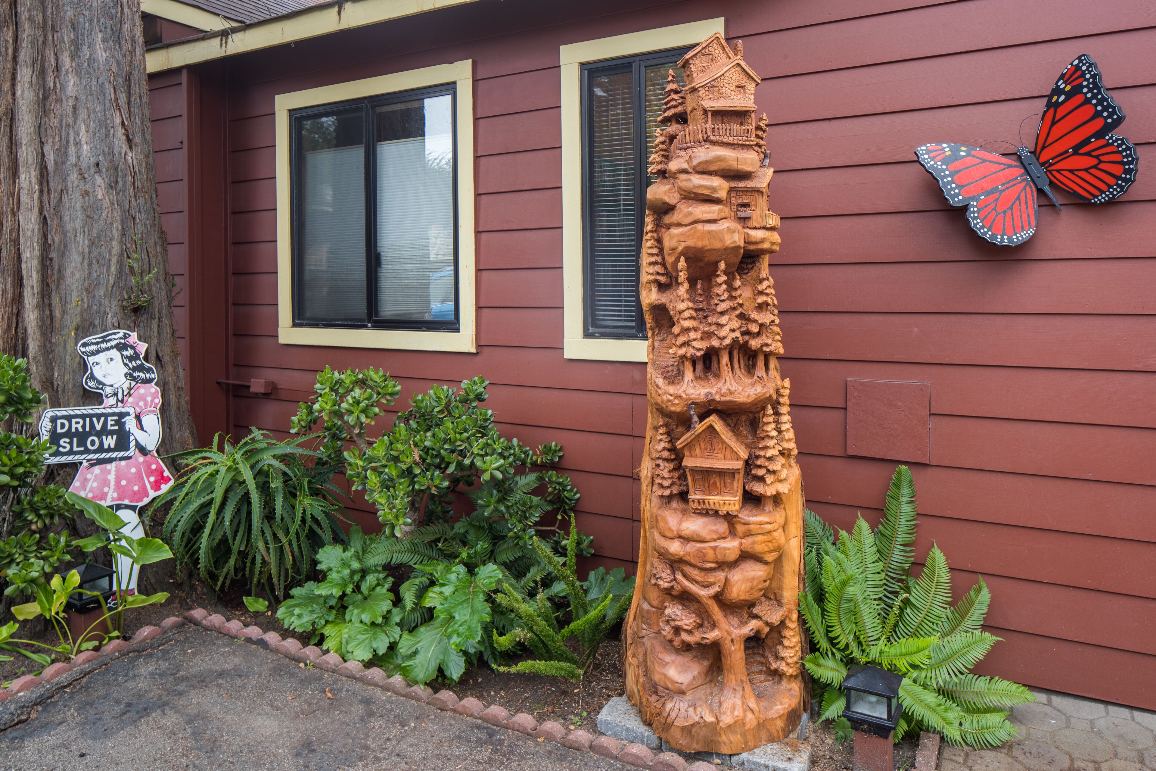 A house with a wooden sculpture, a butterfly decoration, and a 'Drive Slow' sign.