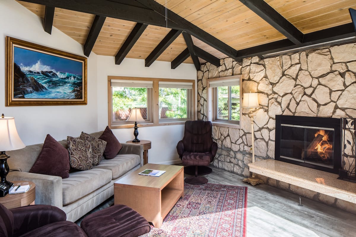 A cozy living room with a stone wall, a fireplace, a sofa, and a painting of the ocean.