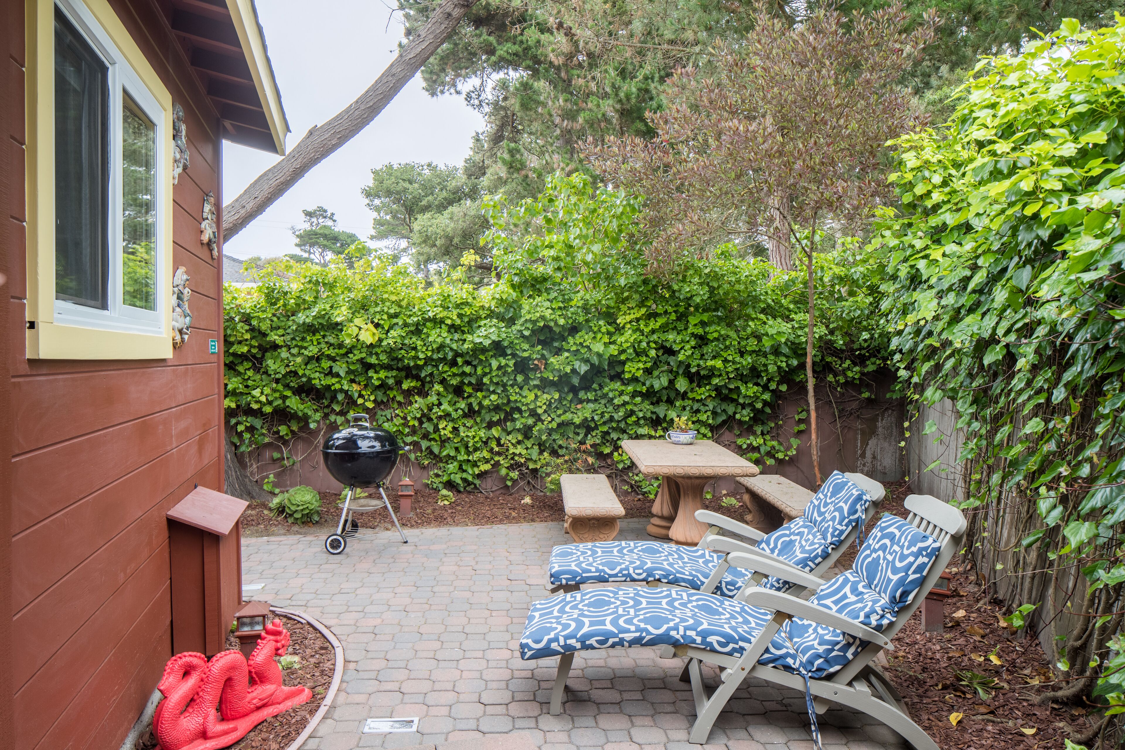 A patio with two blue patterned lounge chairs, a stone table, and a barbecue grill.