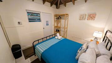 A bedroom with a bed, a window, a door, a shelf, and a lamp.