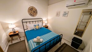 A neatly arranged bedroom with a bed, bedside lamps, a wall-mounted air conditioner, and a mirror. - Waterside Inn (Vieques)