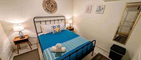A neatly arranged bedroom with a bed, bedside lamps, a wall-mounted air conditioner, and a mirror.