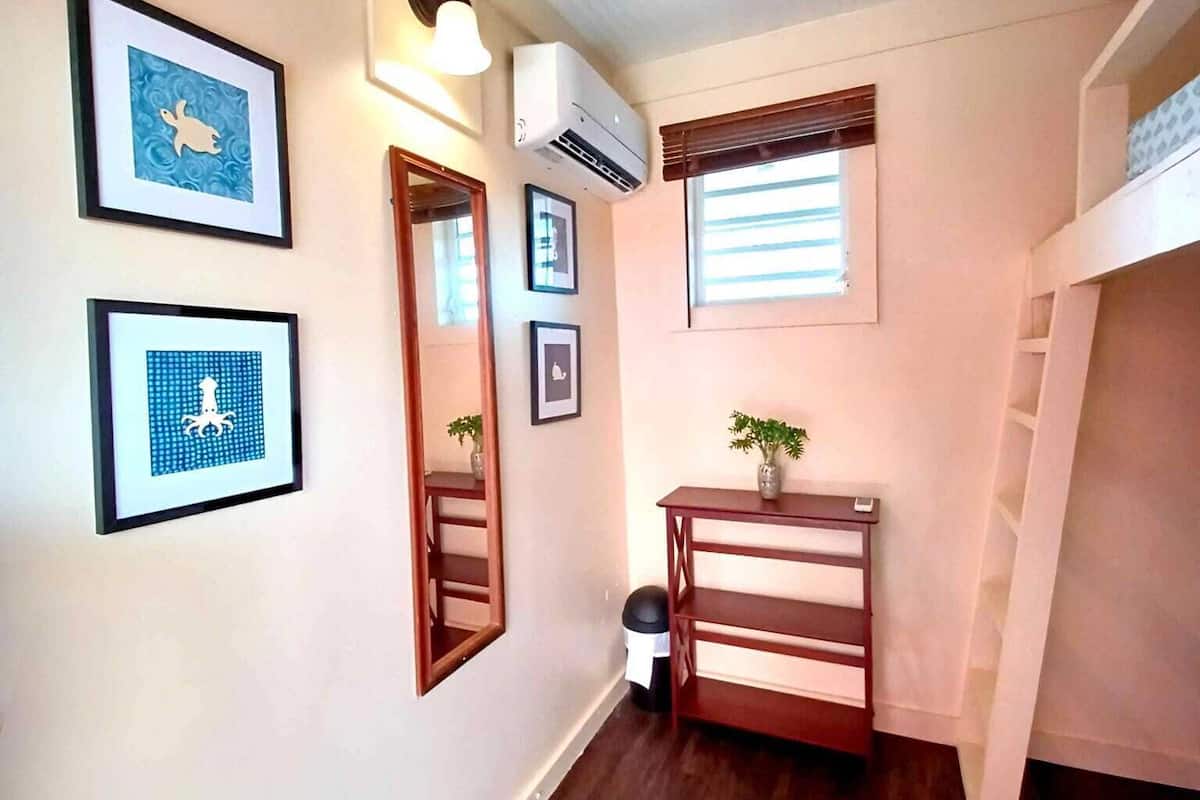 A narrow hallway with wooden flooring, a small table with a plant, and framed artwork on the walls.
