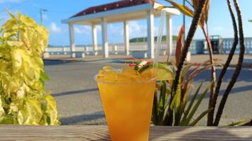 A tropical drink on a wooden table with a view of a beach and a gazebo in the background.