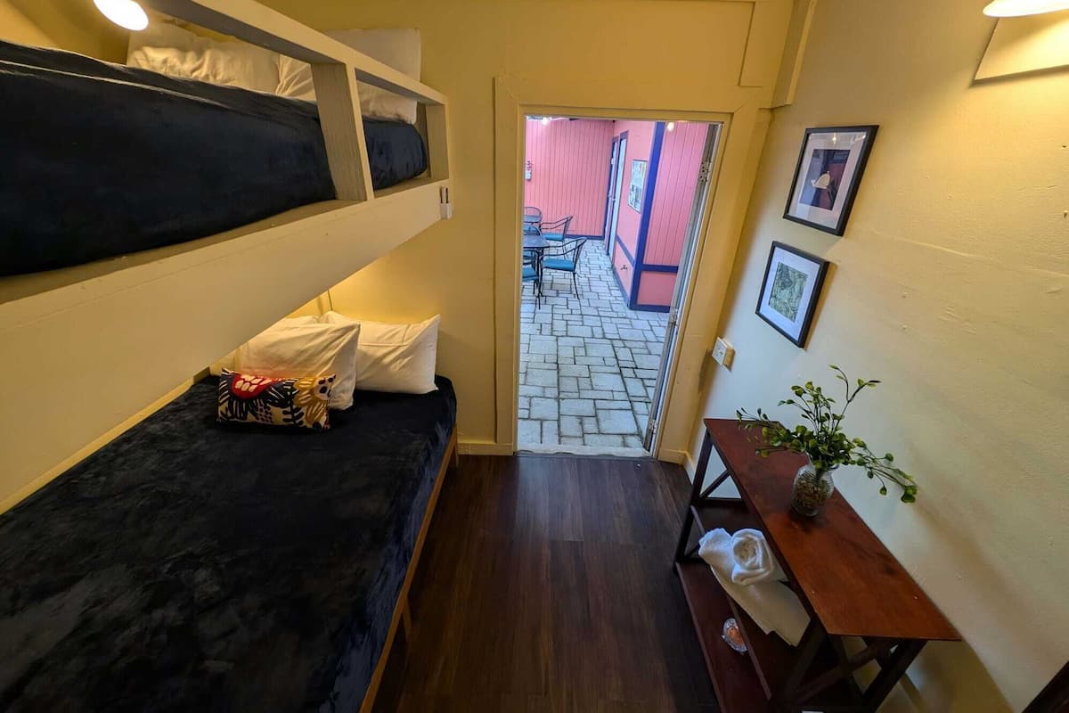 A compact room with a bunk bed, a small table with a plant, and a door leading to an outdoor area with a tiled floor and chairs.