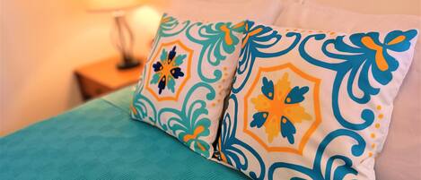 A bed with teal bedding and two decorative pillows with geometric patterns.