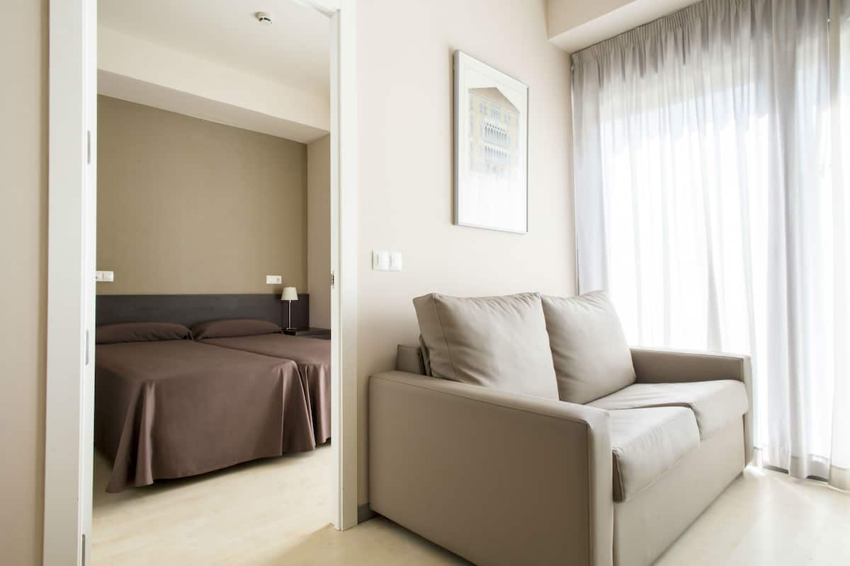 Et moderne hotelværelse med sofa, seng med sengegavl, et indrammet billede på væggen og et vindue med gardiner.
