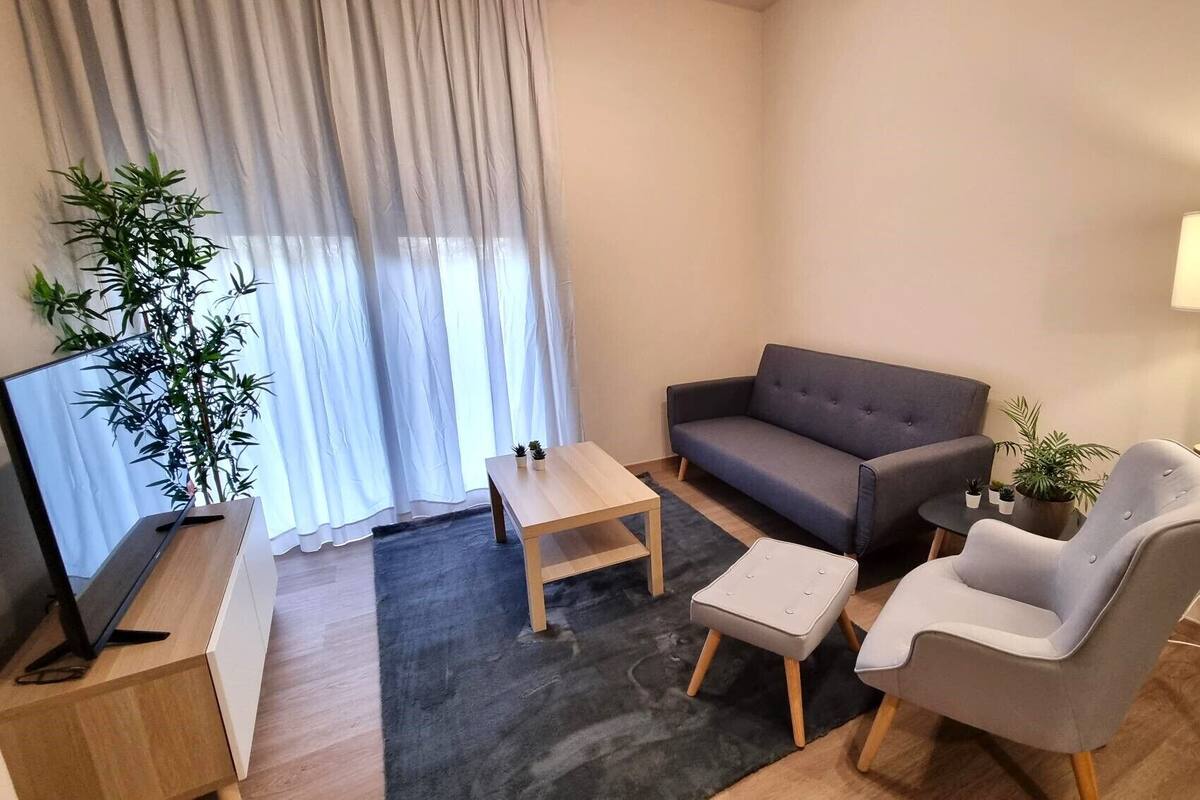 En moderne stue med en sofa, to lænestole, et sofabord, et fjernsyn og en lampe.