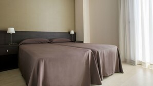 Habitación doble con decoración en tonos neutros, dos mesitas de noche con lámparas y un gran ventanal con cortinas translúcidas.