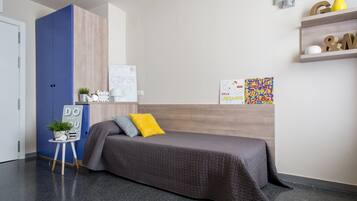 Een moderne slaapkamer met een bed, een blauwe kast, een klein bureau met een plantje en een plank met decoratieve spullen.