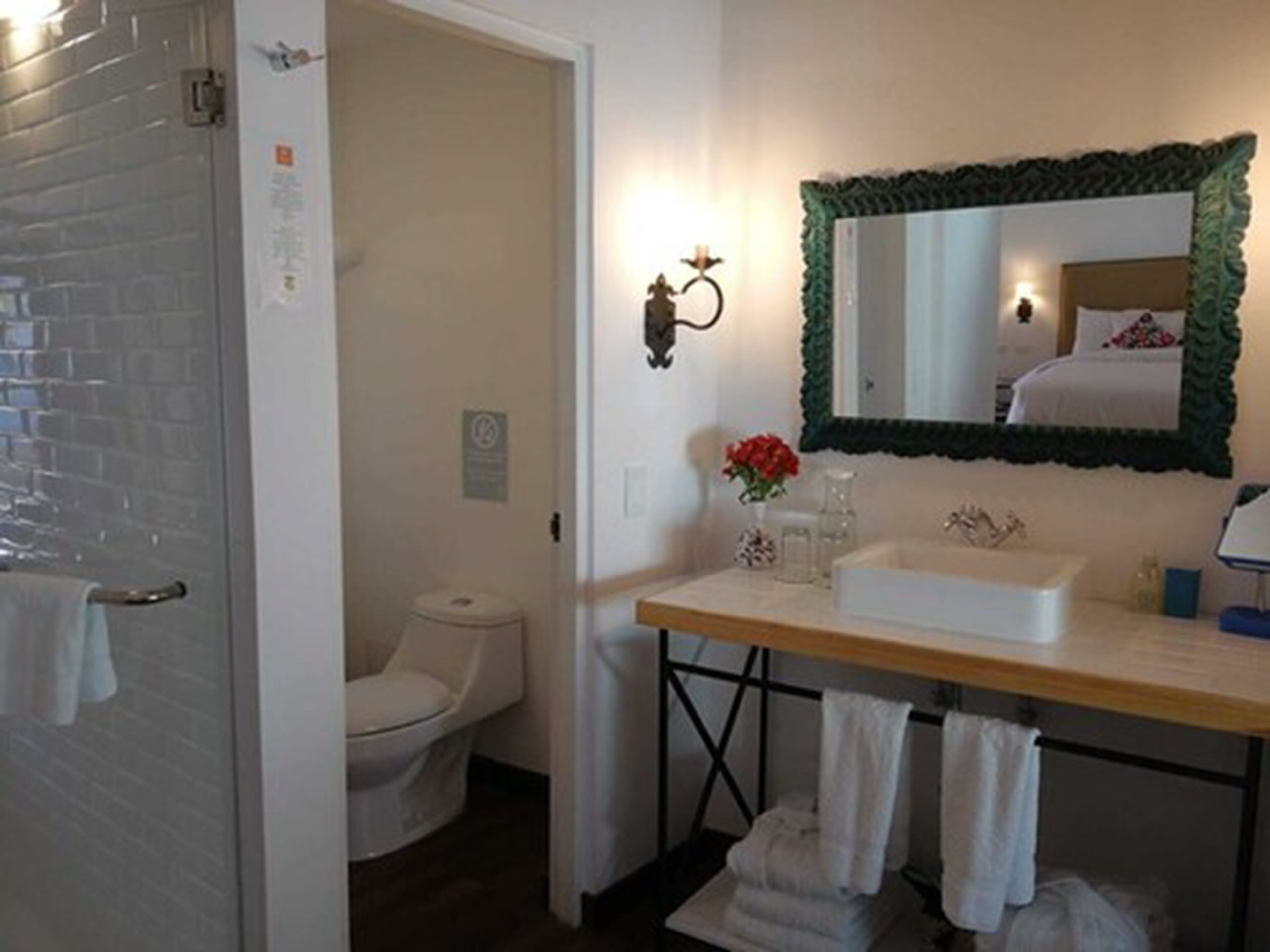Un bagno con un lavandino bianco, uno specchio con cornice verde, un water e una cabina doccia.
