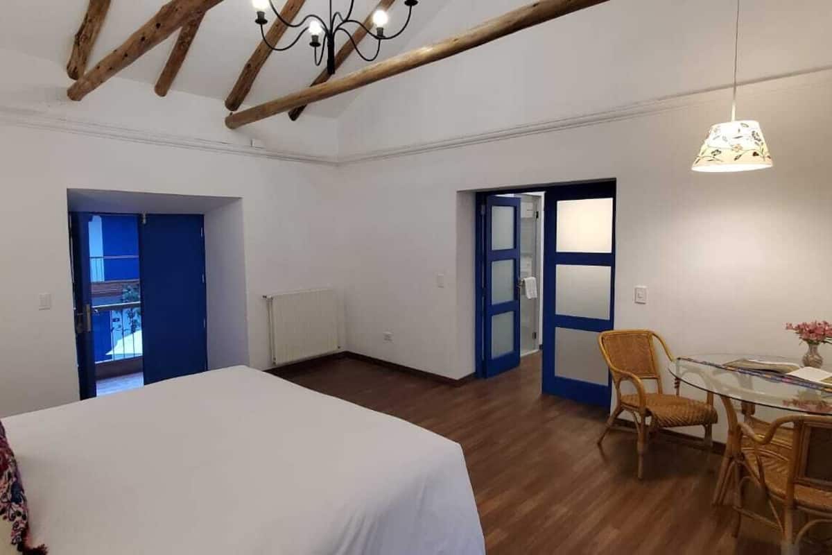 Een slaapkamer met een bed, een glazen tafel met stoelen, en een deur naar een andere kamer.