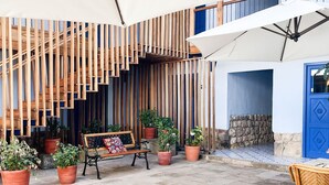 Un espace extérieur aménagé pour prendre les repas, avec une table dressée pour le petit-déjeuner, entourée de chaises en osier, de plantes en pot et d’un mur en bois à lattes.