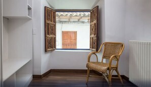 A room with a wooden chair, a window with decorative shutters, and a radiator.