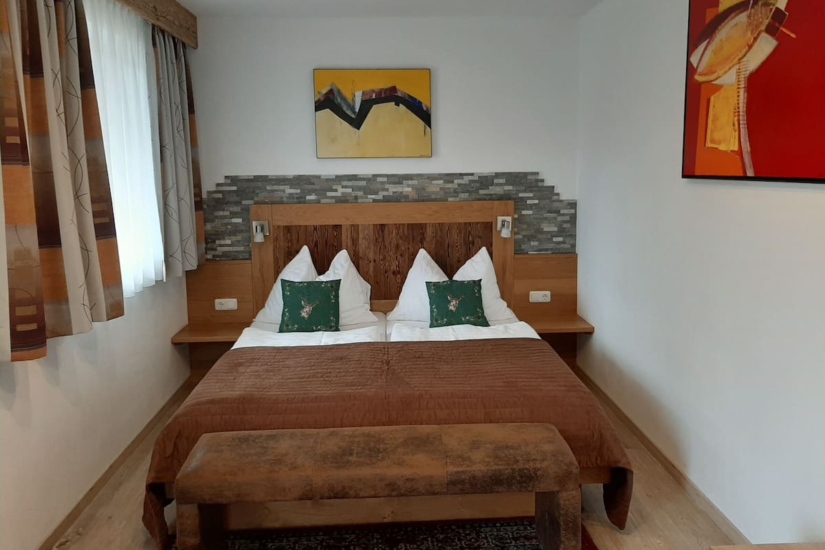 Une chambre à coucher avec une tête de lit en bois, deux oreillers ornés de motifs représentant des têtes de cerf, un lit recouvert d’une courtepointe marron, un banc au pied du lit et un tableau accroché au mur.