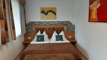 Ein Schlafzimmer mit einem hölzernen Kopfteil, zwei Kissen mit Hirschmotiven, einer Bettdecke in Braun, einer Bank am Fußende des Bettes und einem Gemälde an der Wand.