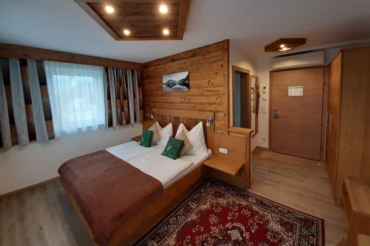 Une chambre à coucher avec une tête de lit en bois, un lit recouvert de draps blancs, des oreillers verts, un tapis à motifs rouges, une table de chevet en bois et une armoire en bois.