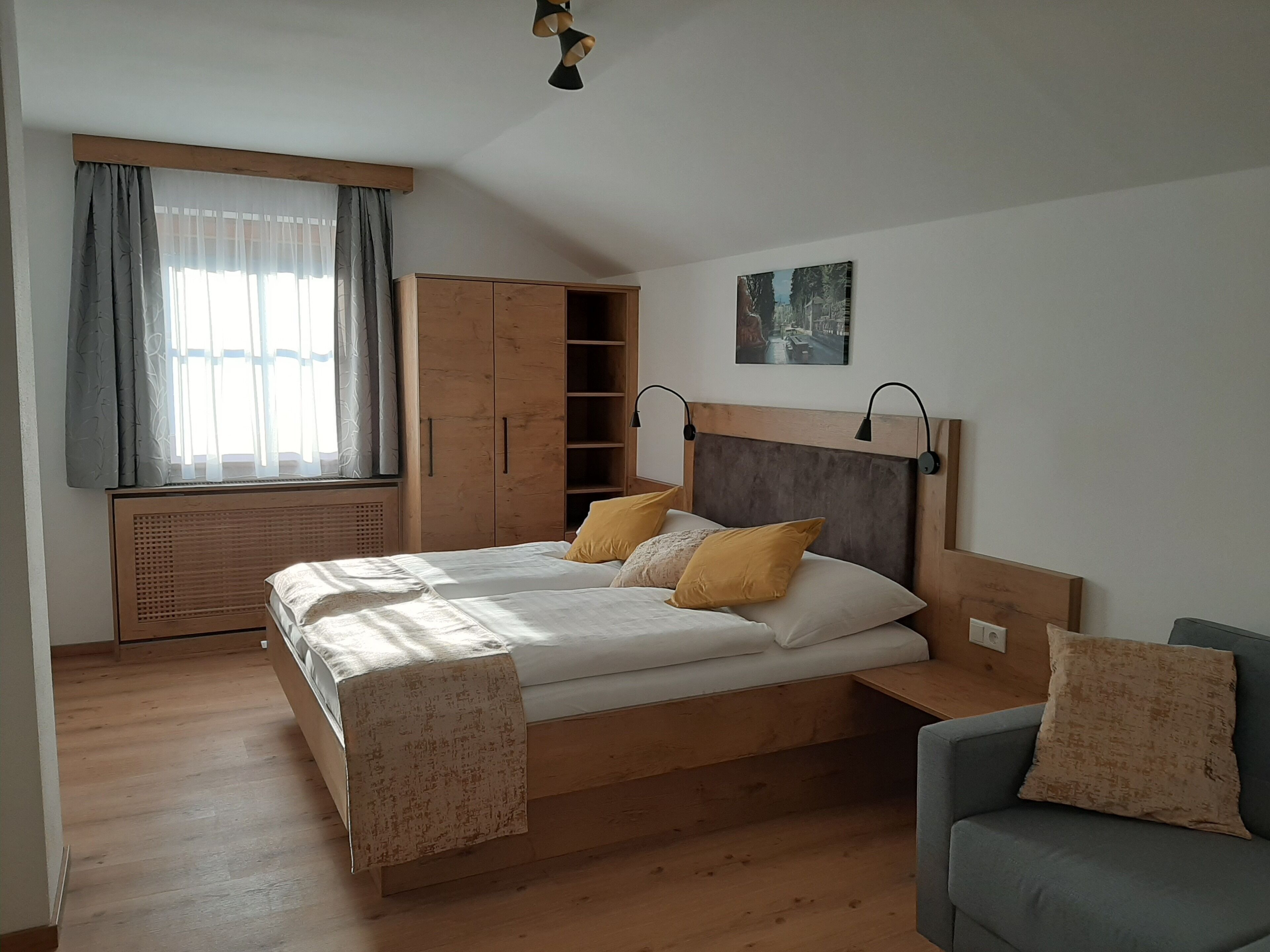 Un dormitorio con una cama de madera, un armario, un radiador y una ventana con cortinas.