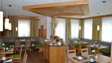 Ein Restaurant mit Holztischen und grün gepolsterten Sitzplätzen, das eine zentrale Insellounge mit einer Blumenvase zeigt.
