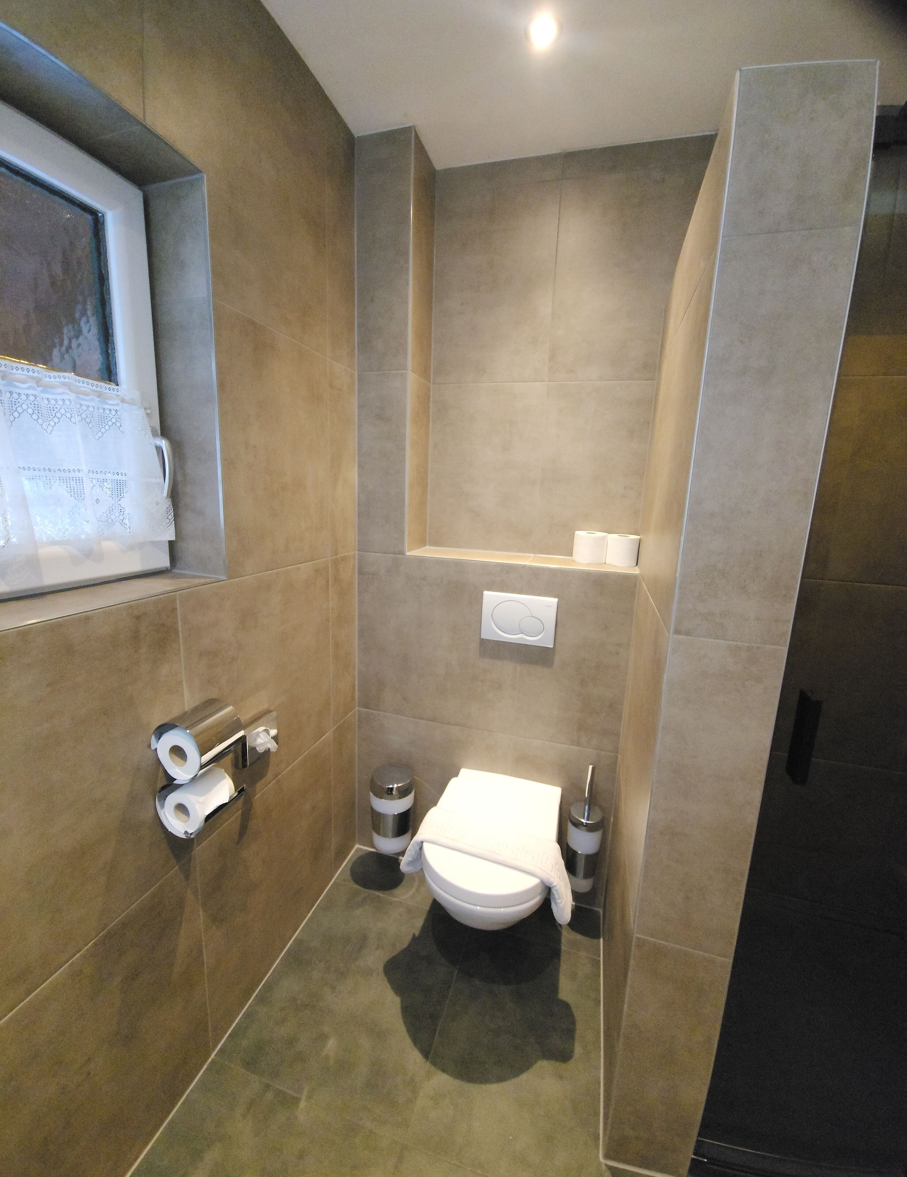 A modern bathroom with a toilet, two paper towel dispensers, a trash bin, and a towel rack.