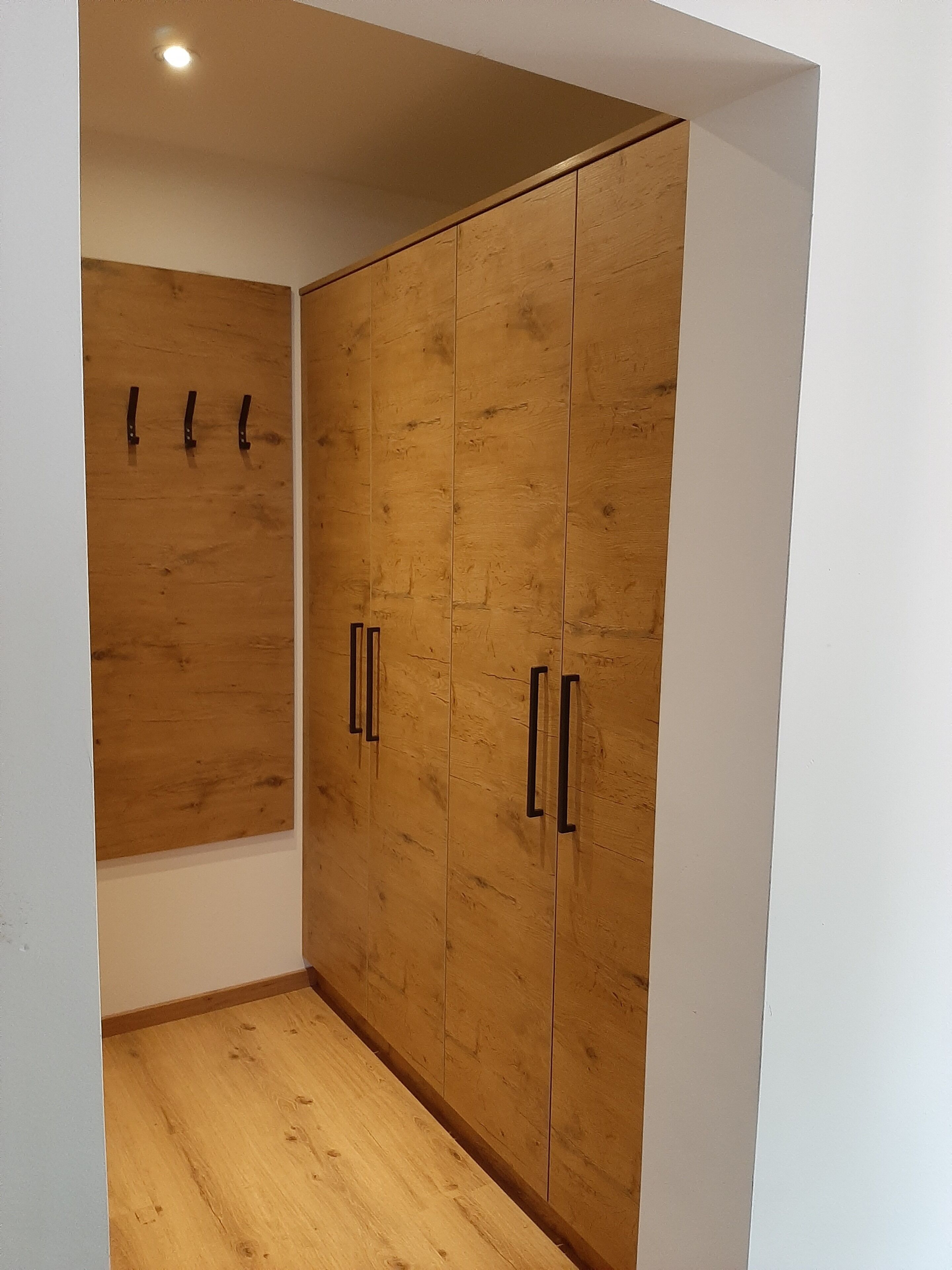 Ein Zimmer mit einem Holzschrank, einer weißen Wand und einem Holzboden.