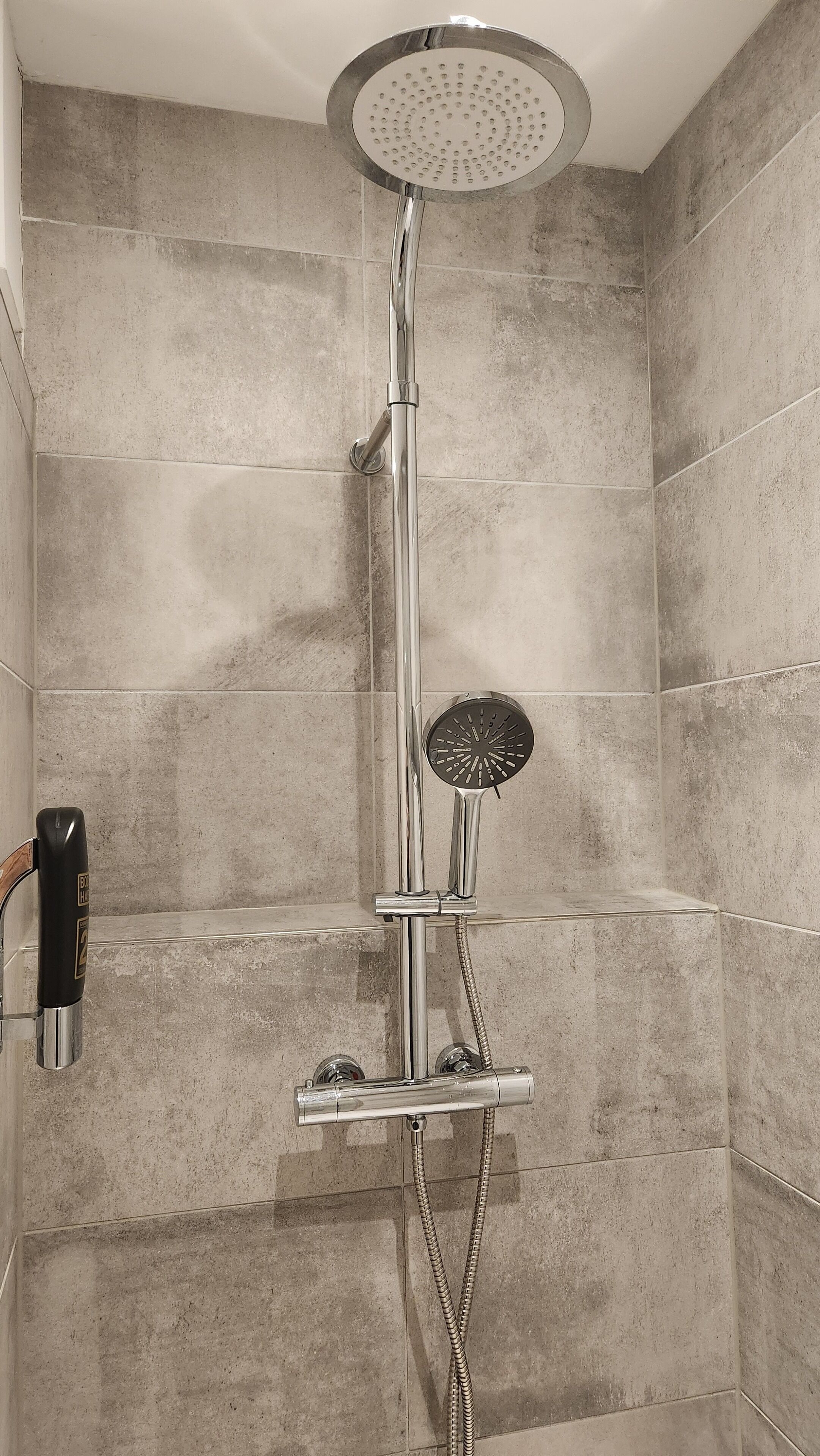 A shower with a handheld showerhead and a handheld scrubber.