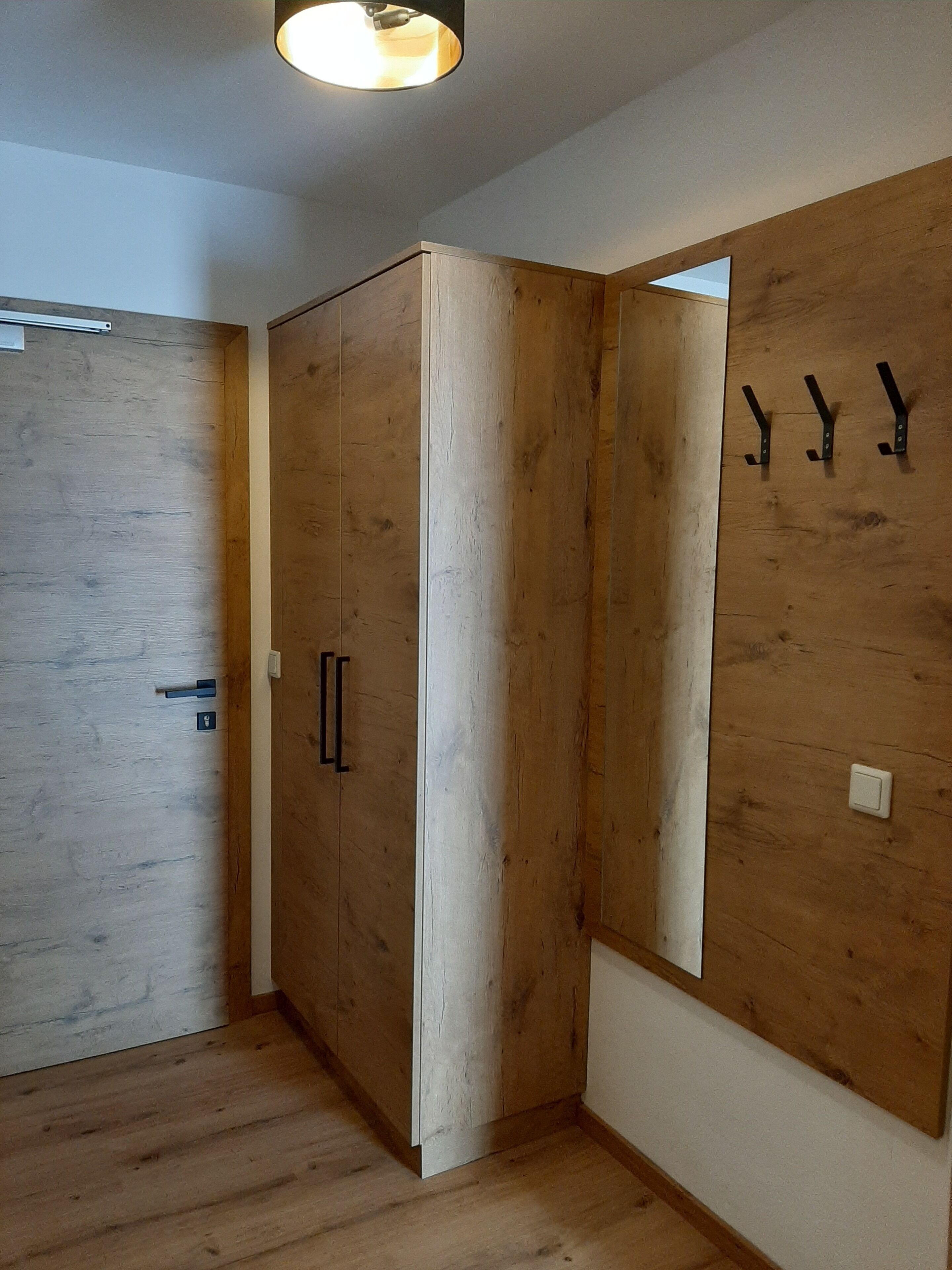 Quarto com piso de madeira, um guarda-roupa espaçoso, um espelho e luminária no teto.