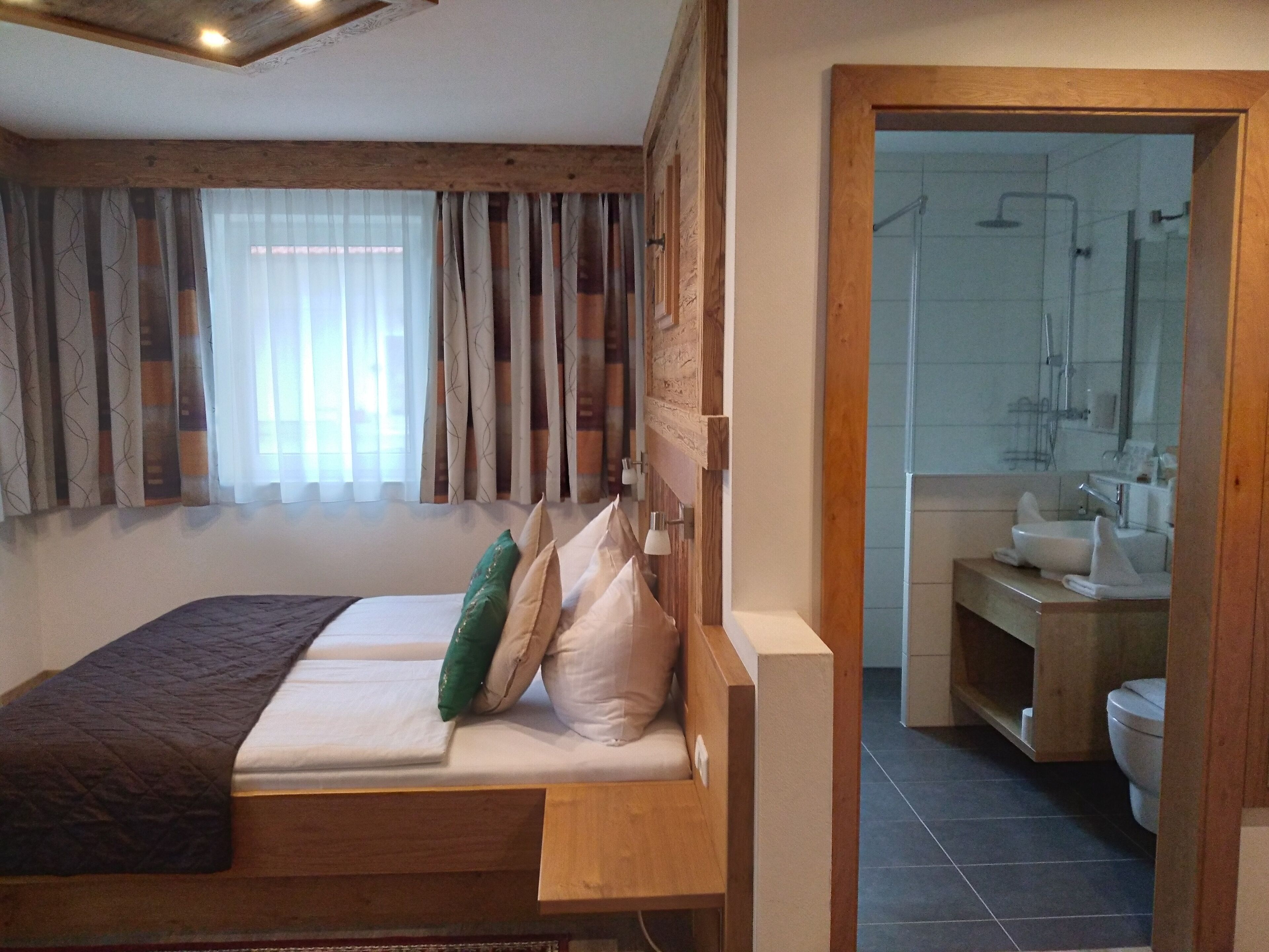 Ein Schlafzimmer mit einem Holz-Kopfteil, einem Bett mit weißen Leinen und Blick auf ein Badezimmer mit Dusche und Waschbecken.